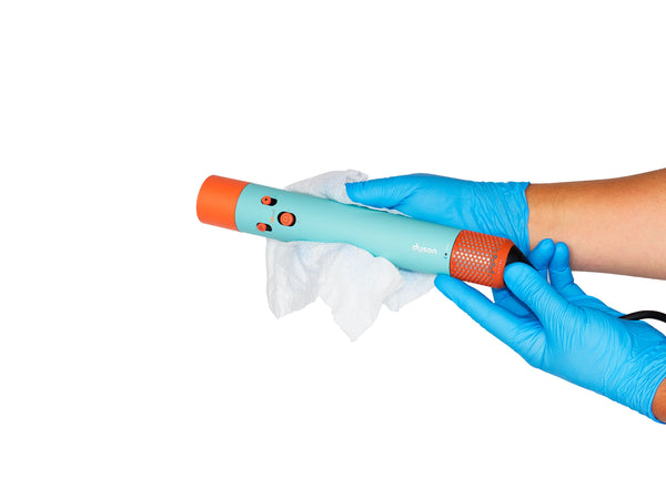 Two hands in nitrile gloves cleaning a Dyson Airwrap with a sanitization wipe