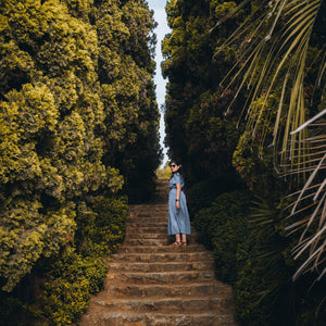 Traveler in a striped blue dress on stone garden steps lined with cypress trees in Europe